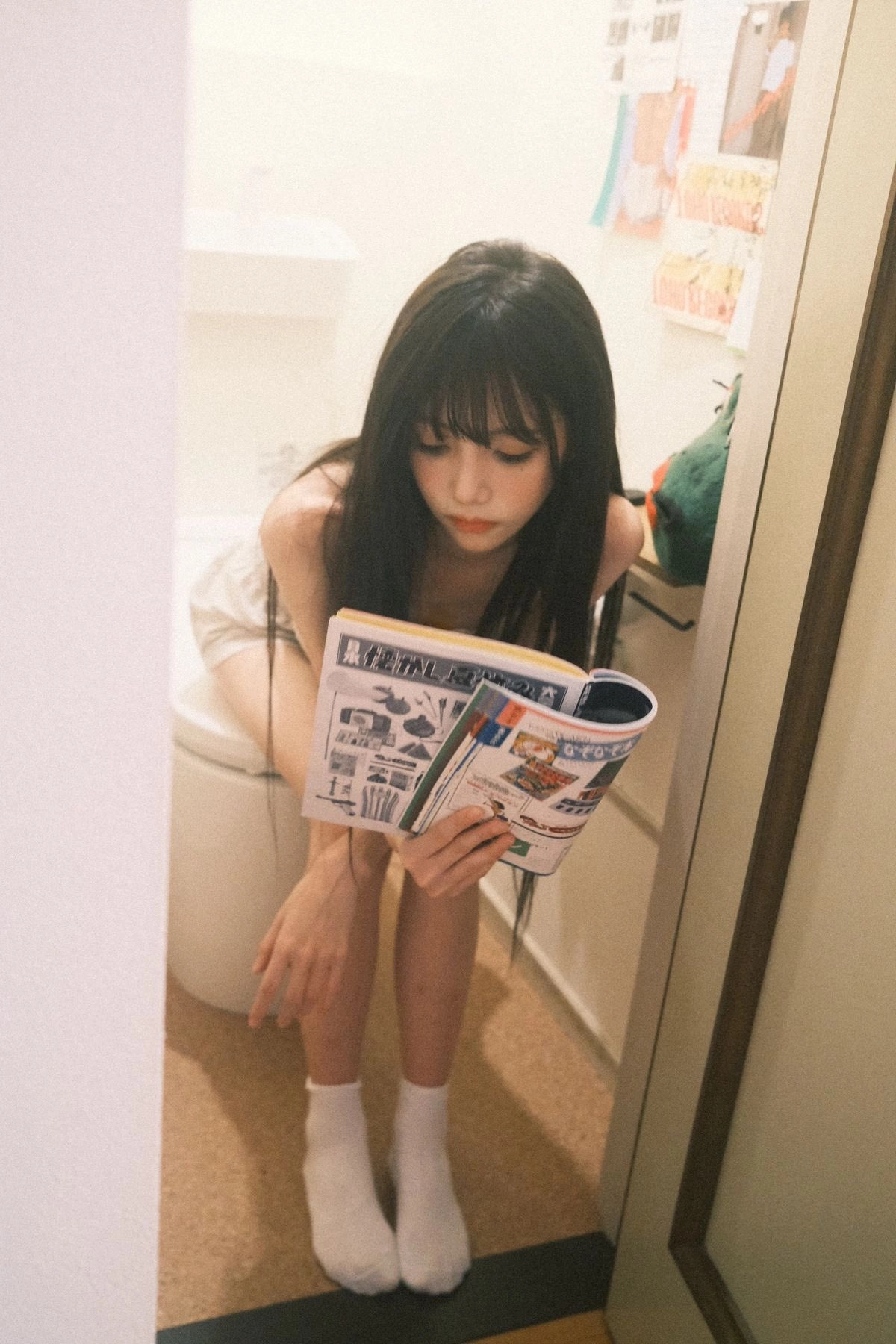 A girl sits in the toilet reading a magazine.