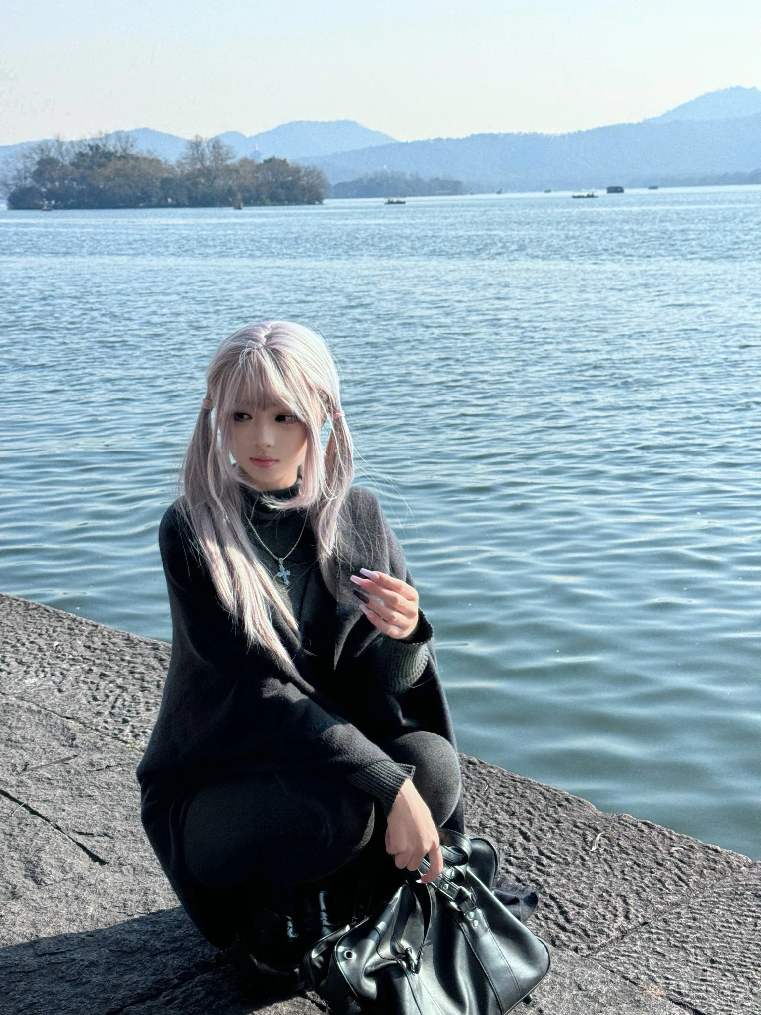 一个长头发的女人坐在水边的岩石上。