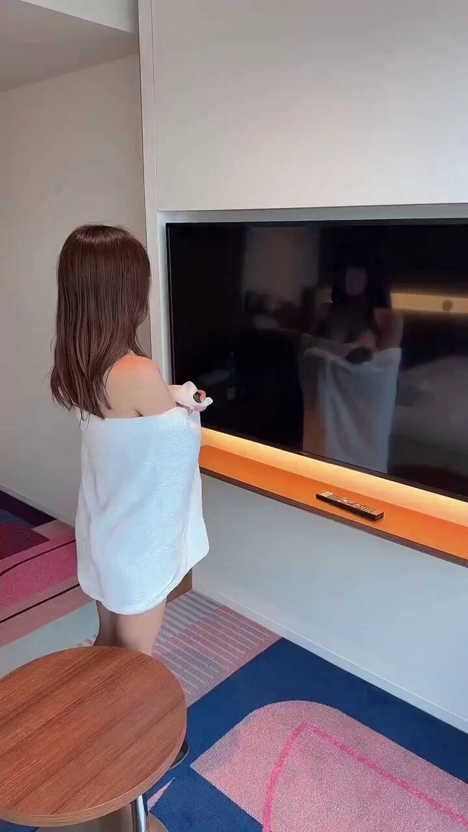 穿着白毛巾的女人站在一台平面电视前。