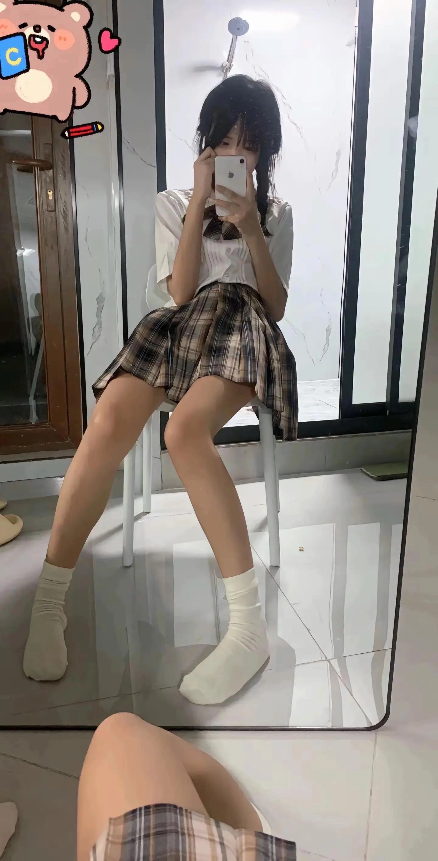 一位穿着白色衬衫和裙的女人坐在椅子上,看着她的手机。