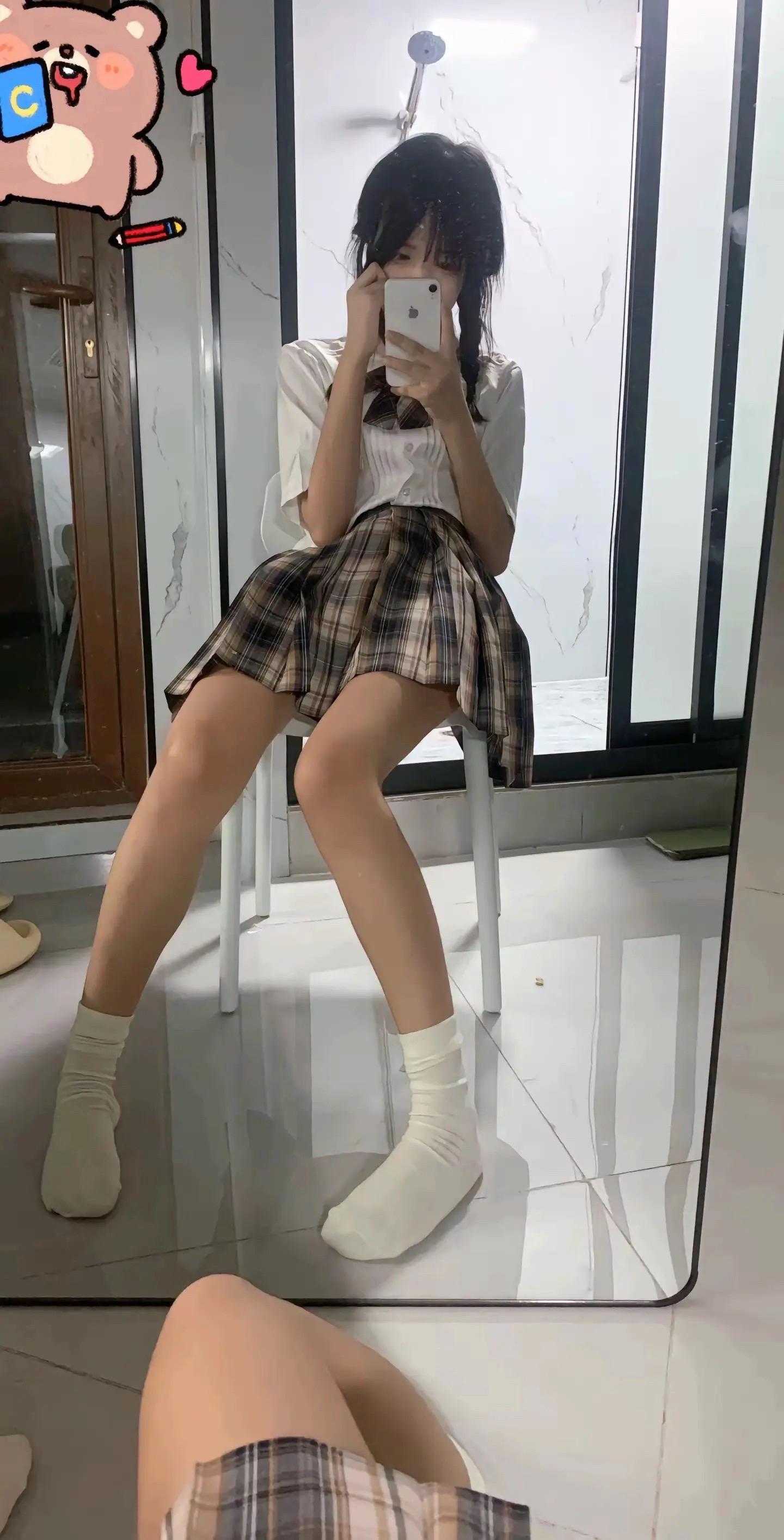 一位穿着白色衬衫和裙的女人坐在椅子上,看着她的手机。