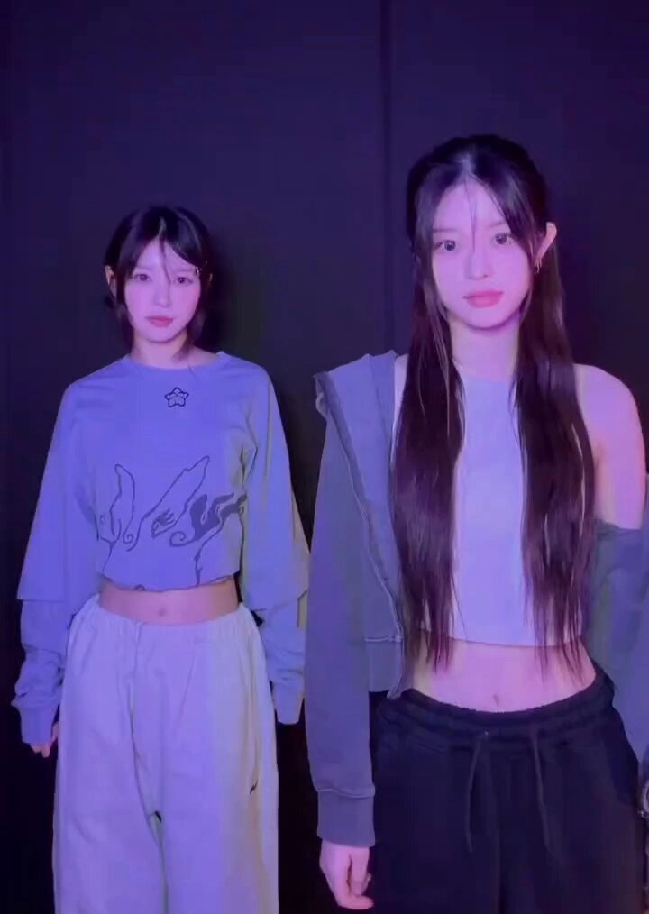 两个女孩在房间里,一个穿着蓝色衬衫,另一个穿着灰色衬衫。