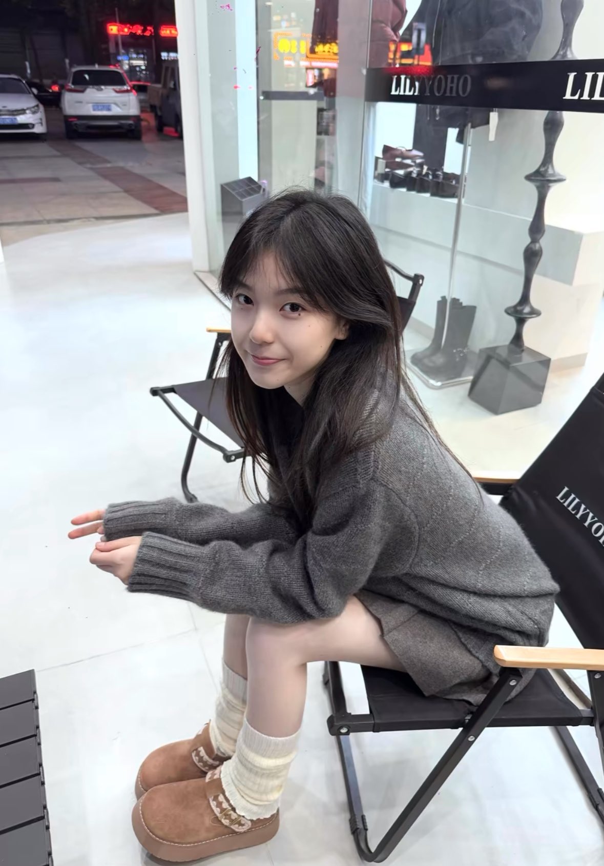 女人坐在一把灰色衬衫和黑色鞋子的椅子上。