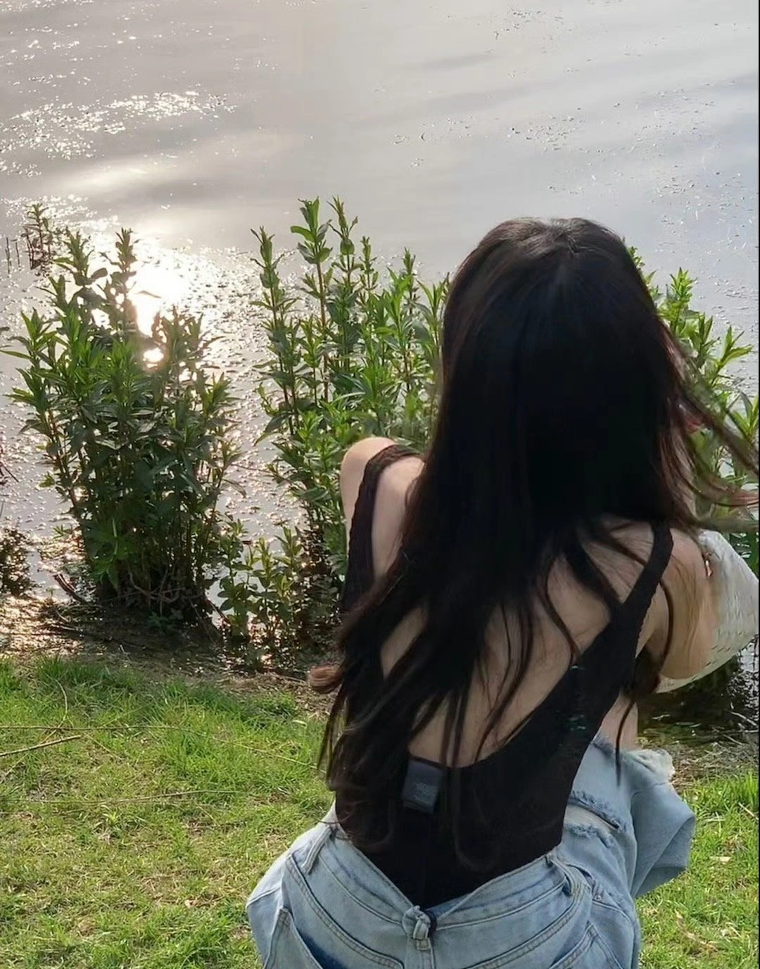 穿着黑色坦克顶的女人坐在湖边的草地上。