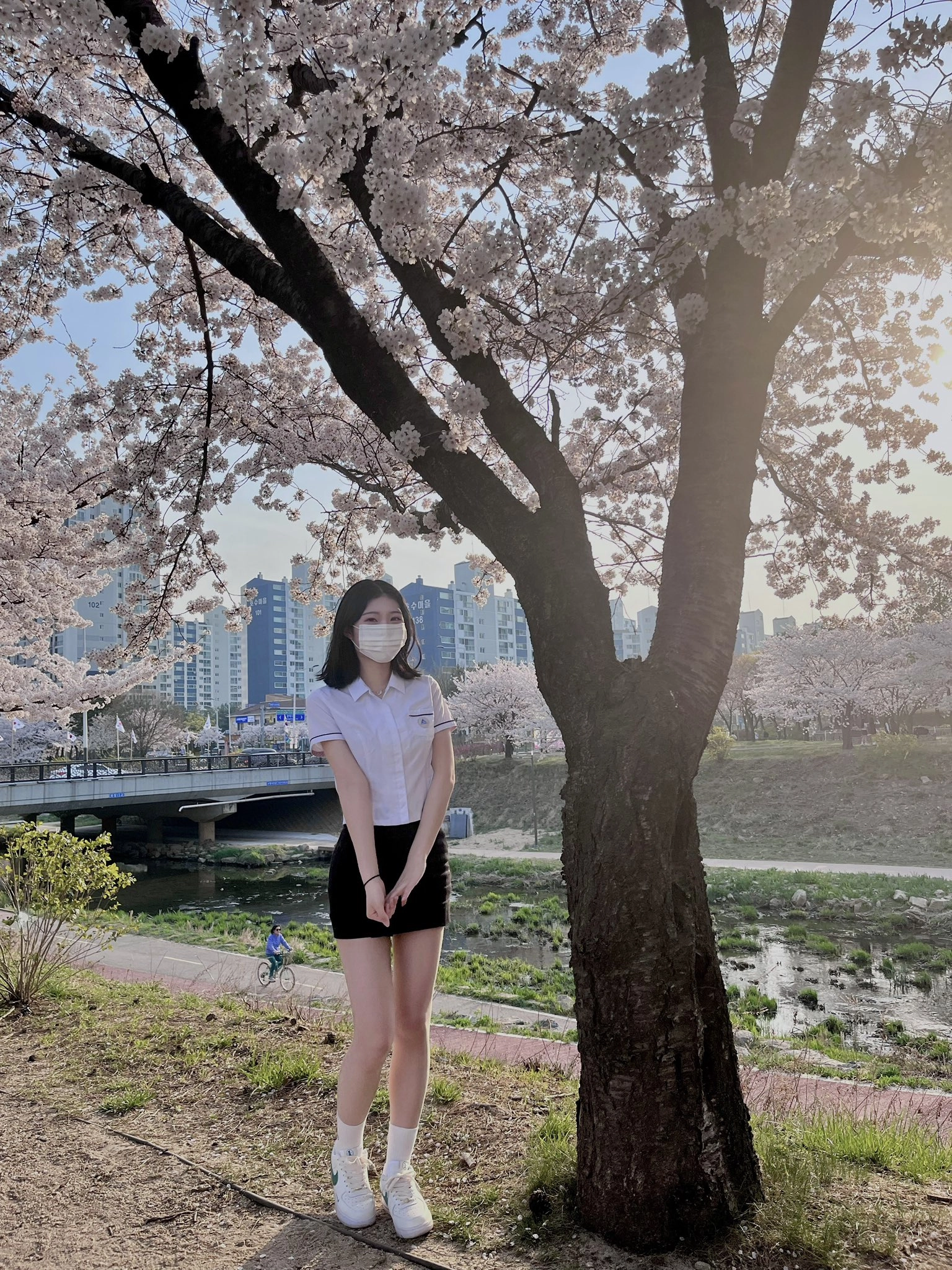 一位戴着面具的女人站在一棵带花的树下。