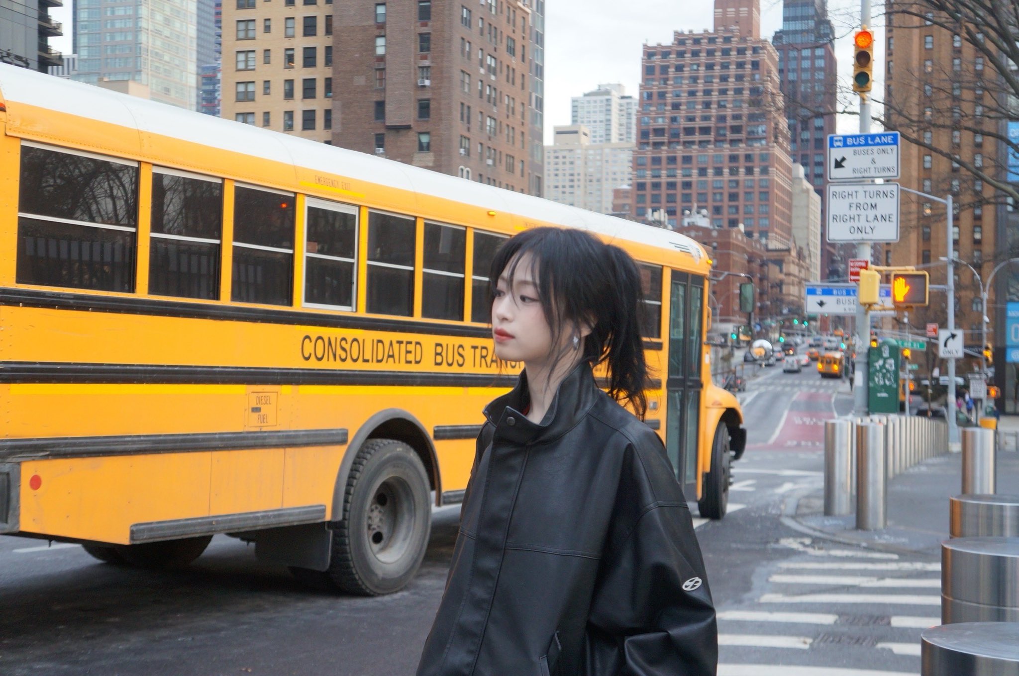 一位穿着黑色皮革夹克和黑色头发的女人站在城市街上。