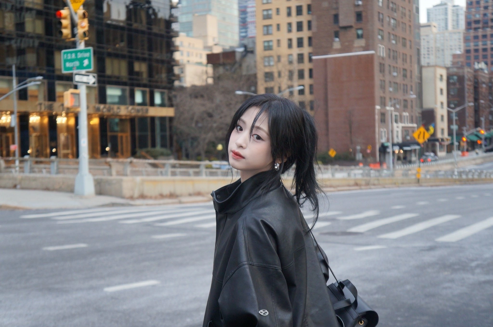 一位穿着黑色皮革夹克和黑色头发的女人站在城市街上。