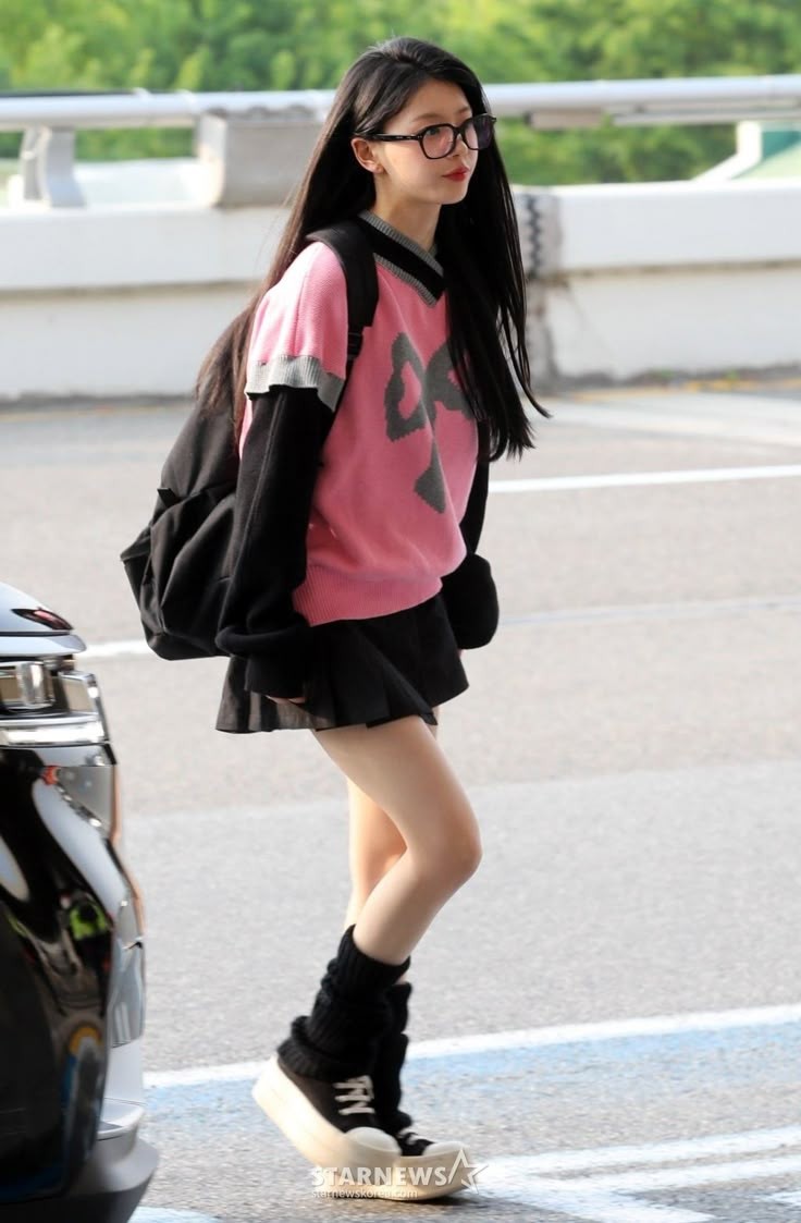 一位穿着粉红色衬衫和黑色裙子的女孩走在街上。