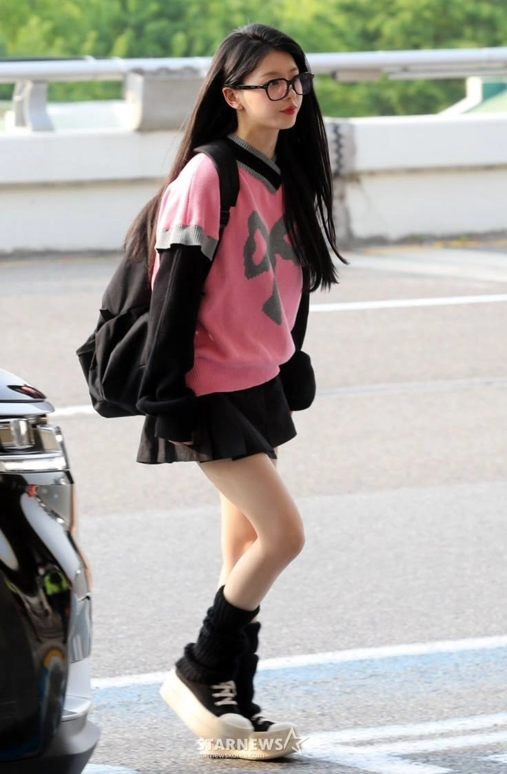 一位穿着粉红色衬衫和黑色裙子的女孩走在街上。