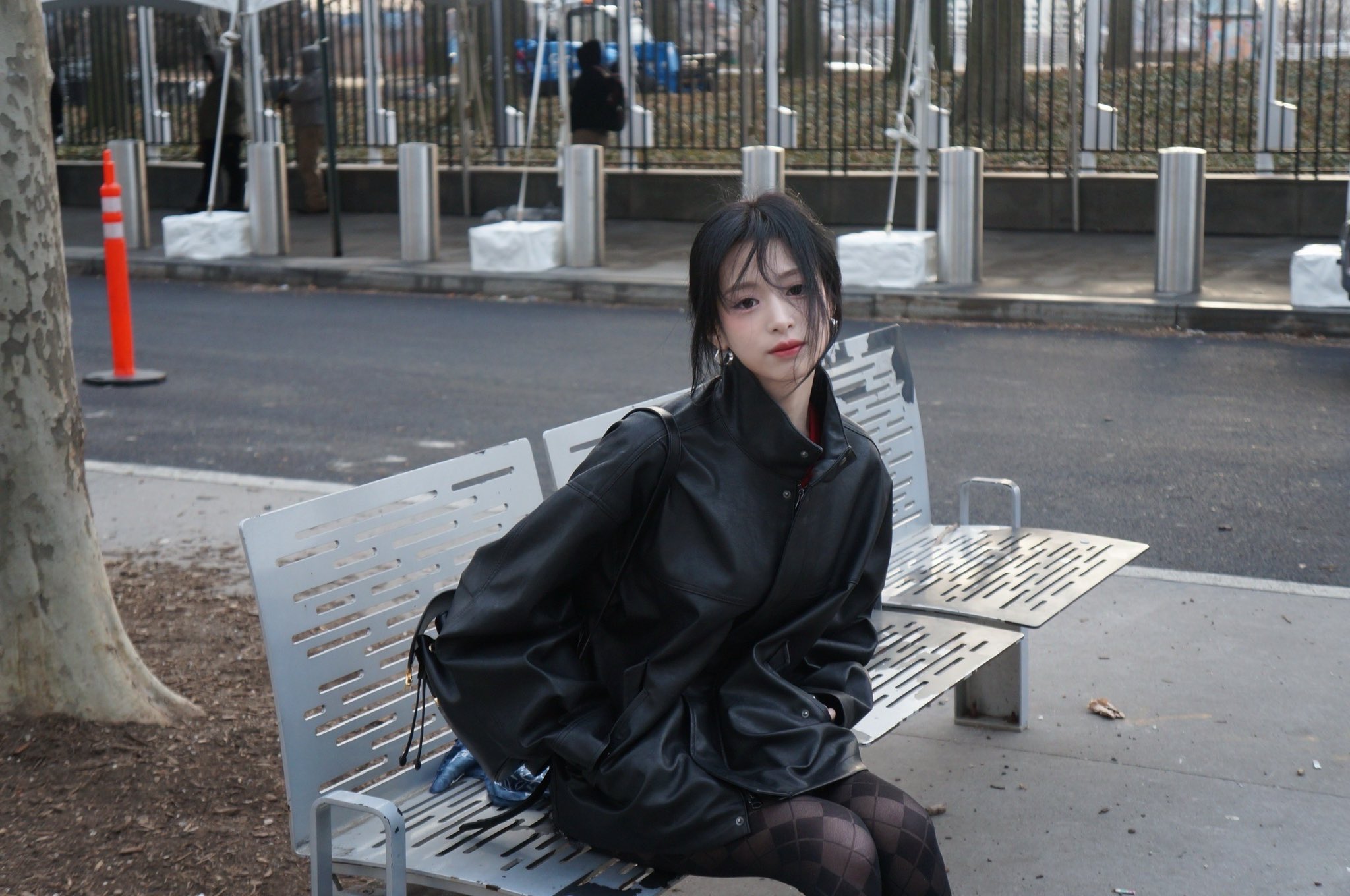 一位穿着黑色皮革夹克和黑色头发的女人站在城市街上。