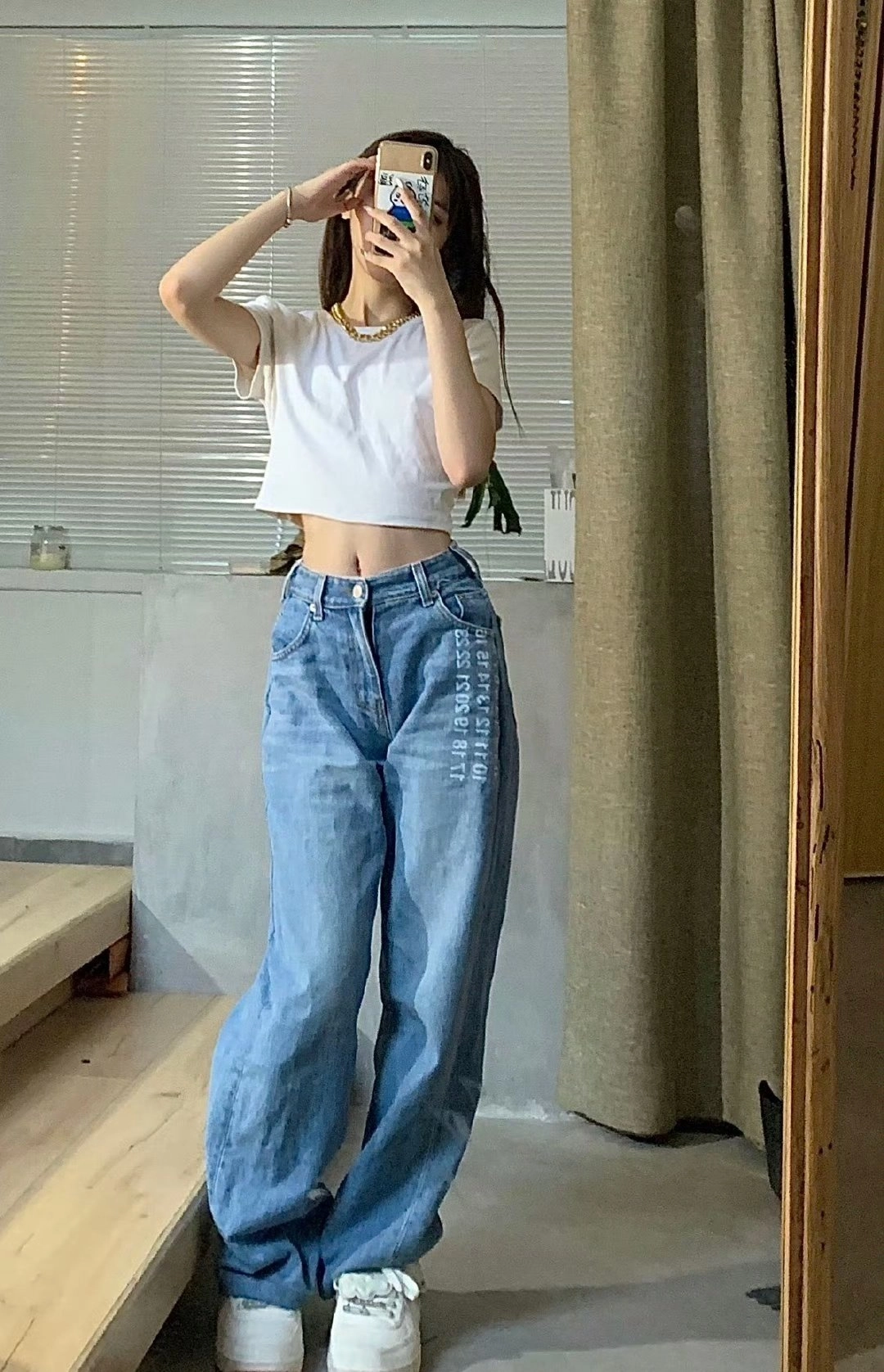 一位穿着白色衬衫和蓝色牛仔裤的女人在镜子前拍自拍。