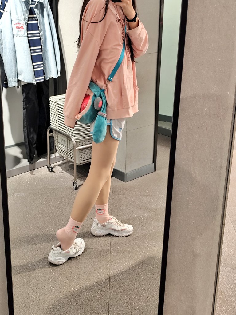 穿着粉红色夹克和蓝色短裤的女人正在镜子里拍照。