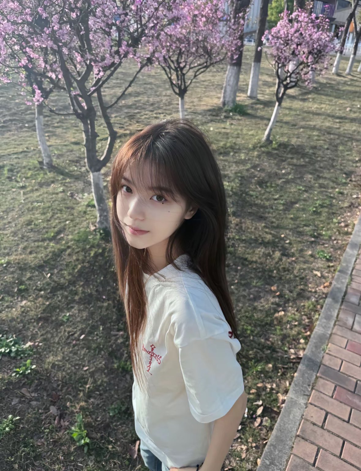 长头发和白衬衫的女人站在一棵树前。