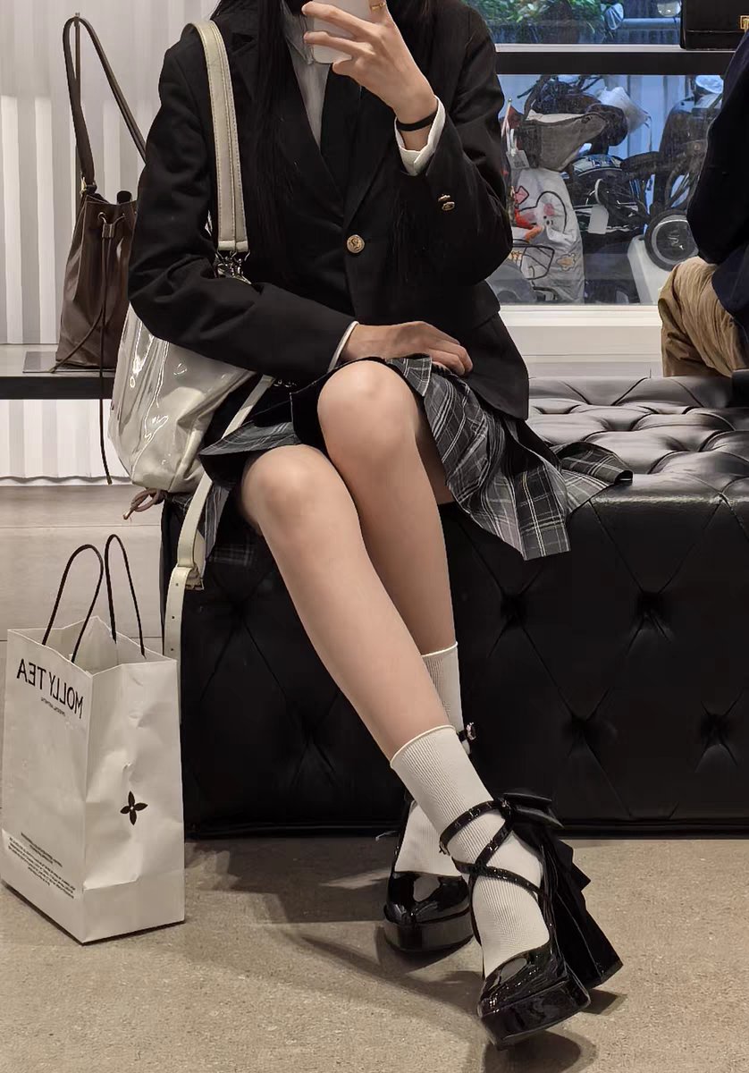 穿着黑色夹克和白色袜子的女人坐在一个凳子上。