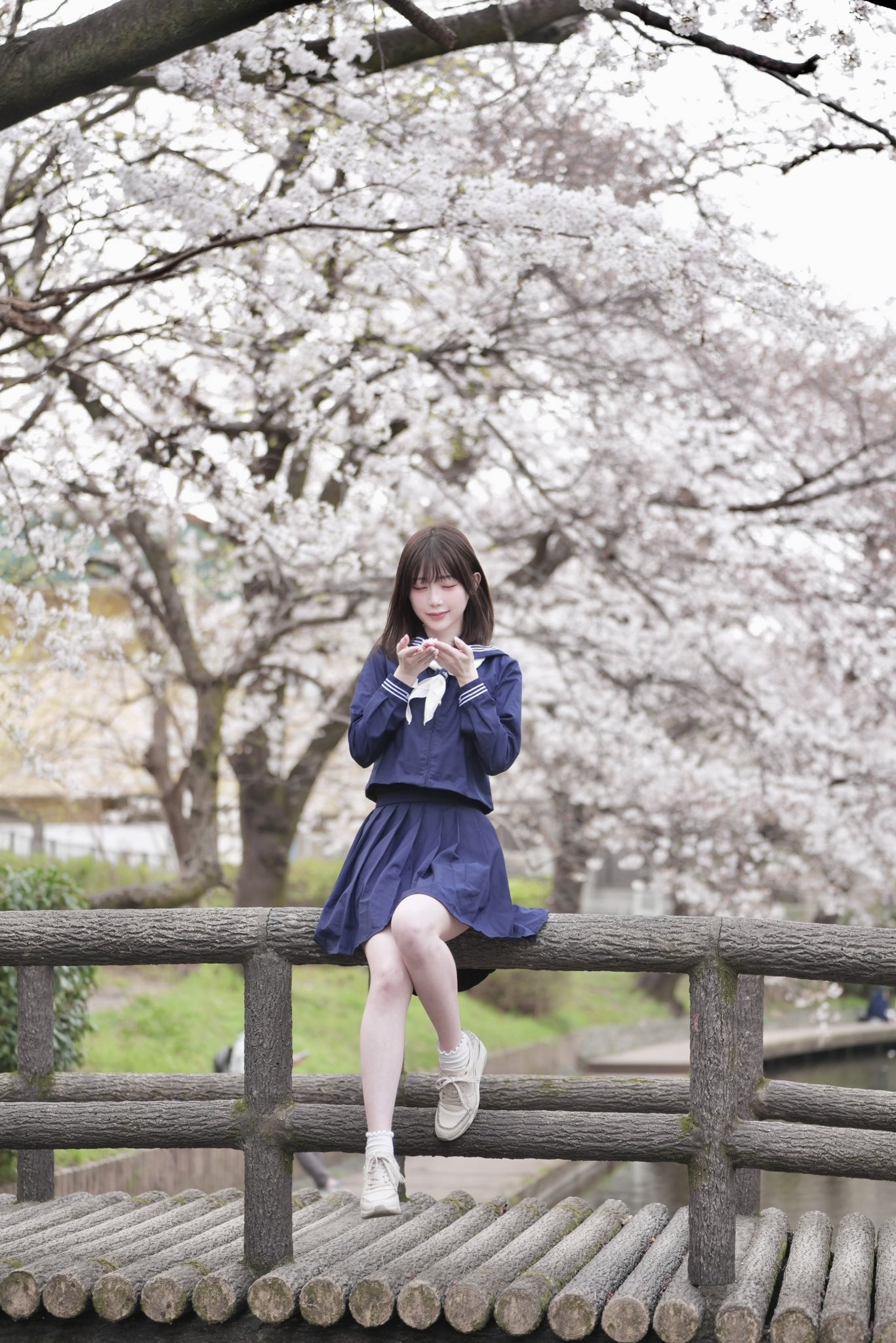 女人坐在一个围栏上,身着蓝色裙子和白色的鞋子。