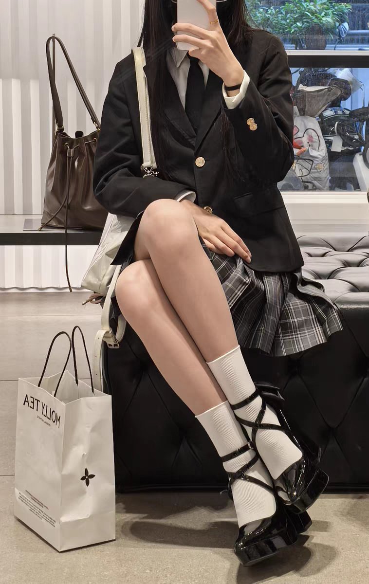 穿着黑色夹克和白色袜子的女人坐在一个凳子上。