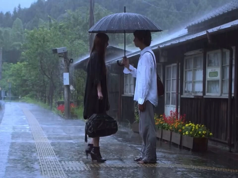 男人和一个女人站在雨中的伞下。