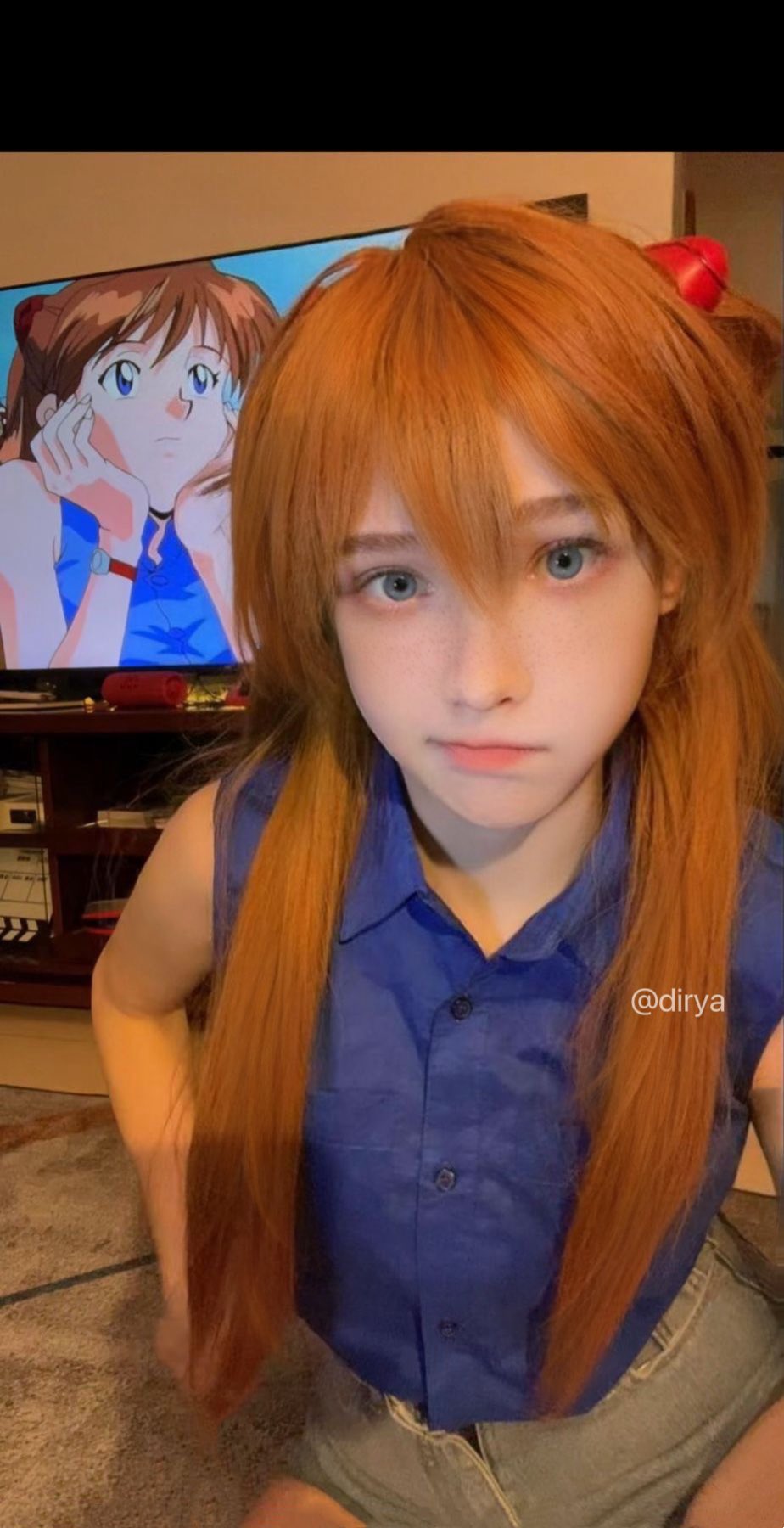 长头发和蓝衬衫的女孩站在电视机前。