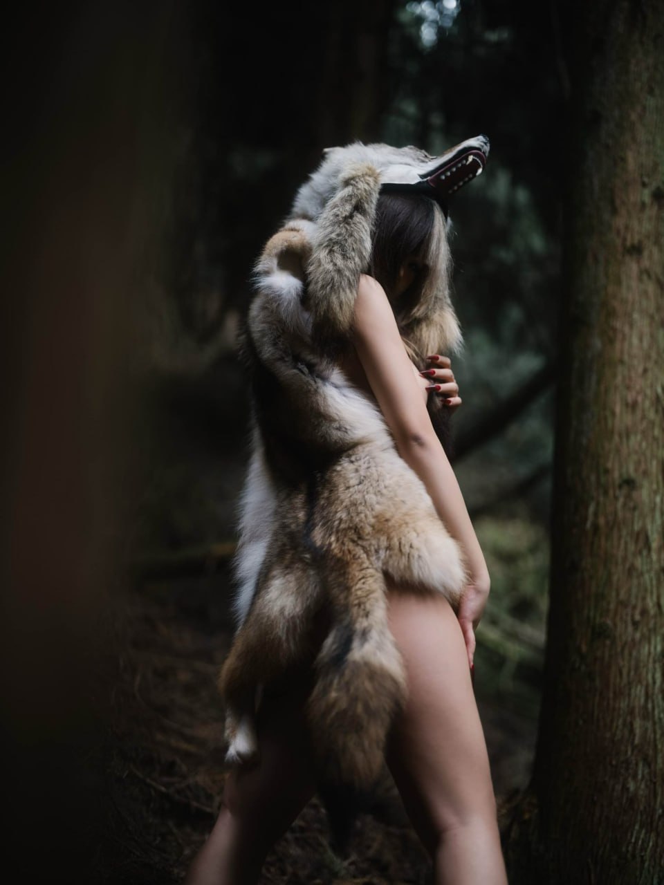 戴着狼帽的女人坐在树林里。