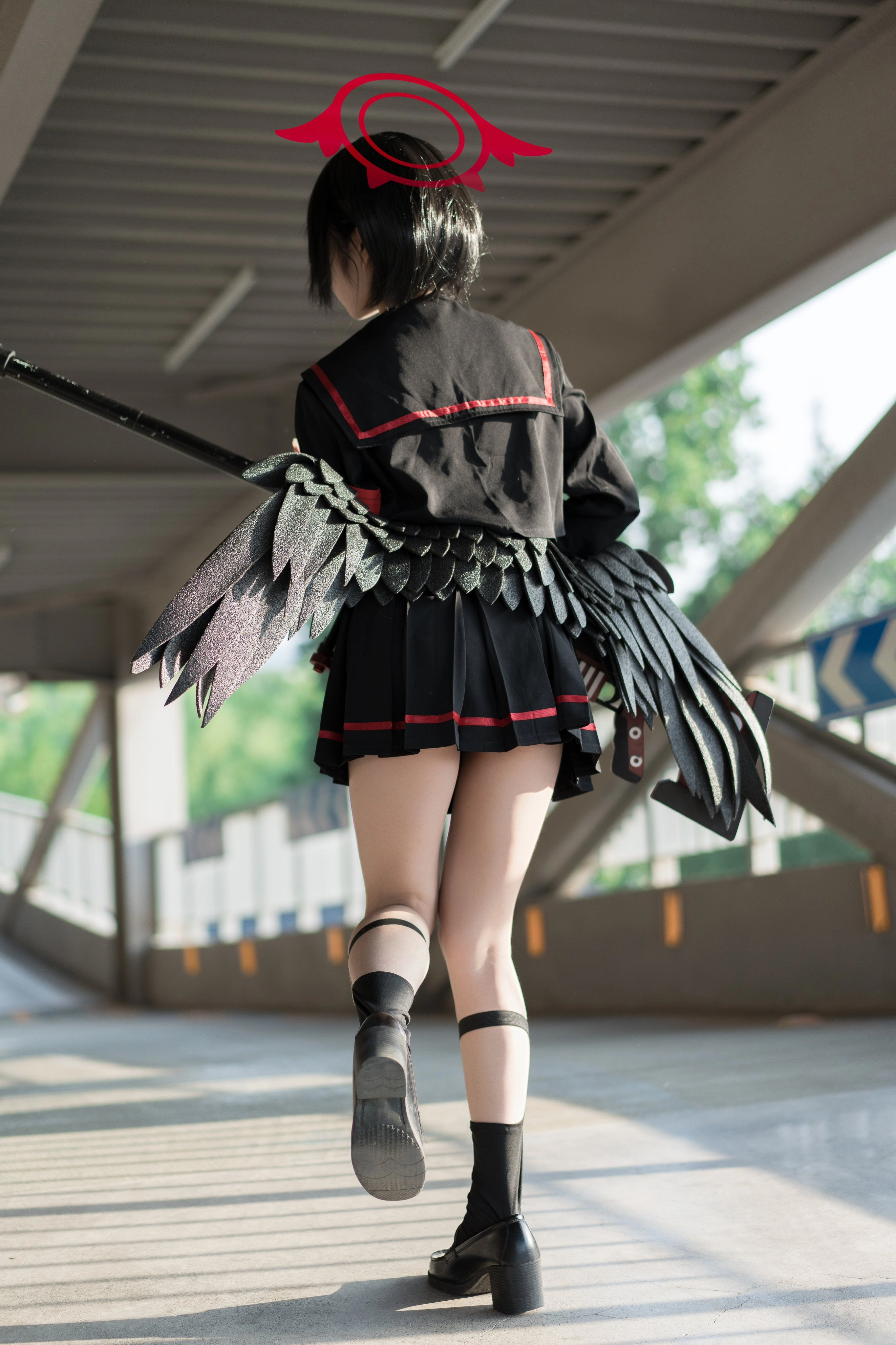 一位穿着黑色和红色的衣服和黑色的翅膀的女人走在一座桥上。