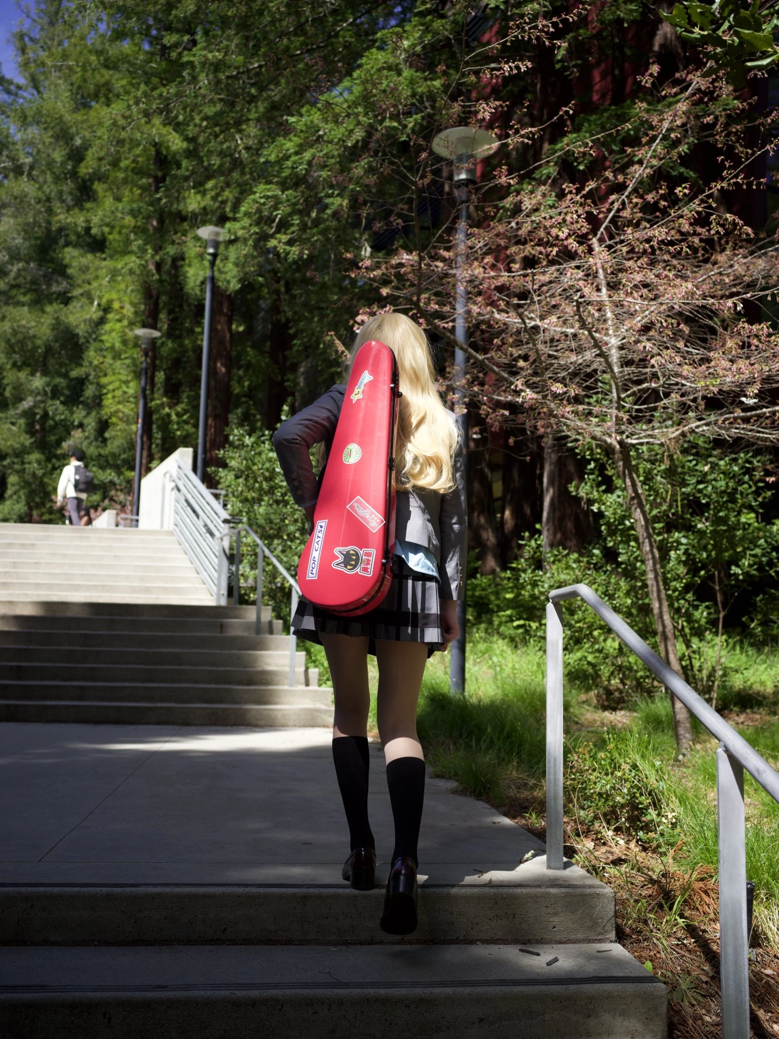 一位带着红色吉他盒子的女人走下了一段楼梯。