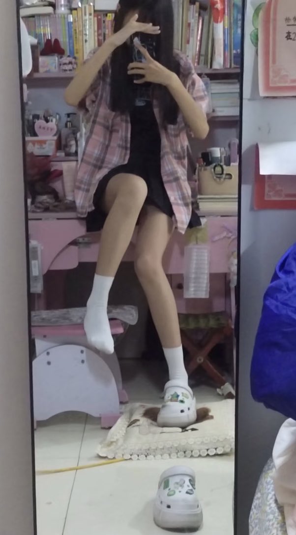 一位穿着黑色裙子和白色袜子的女孩正在镜子里拍照。