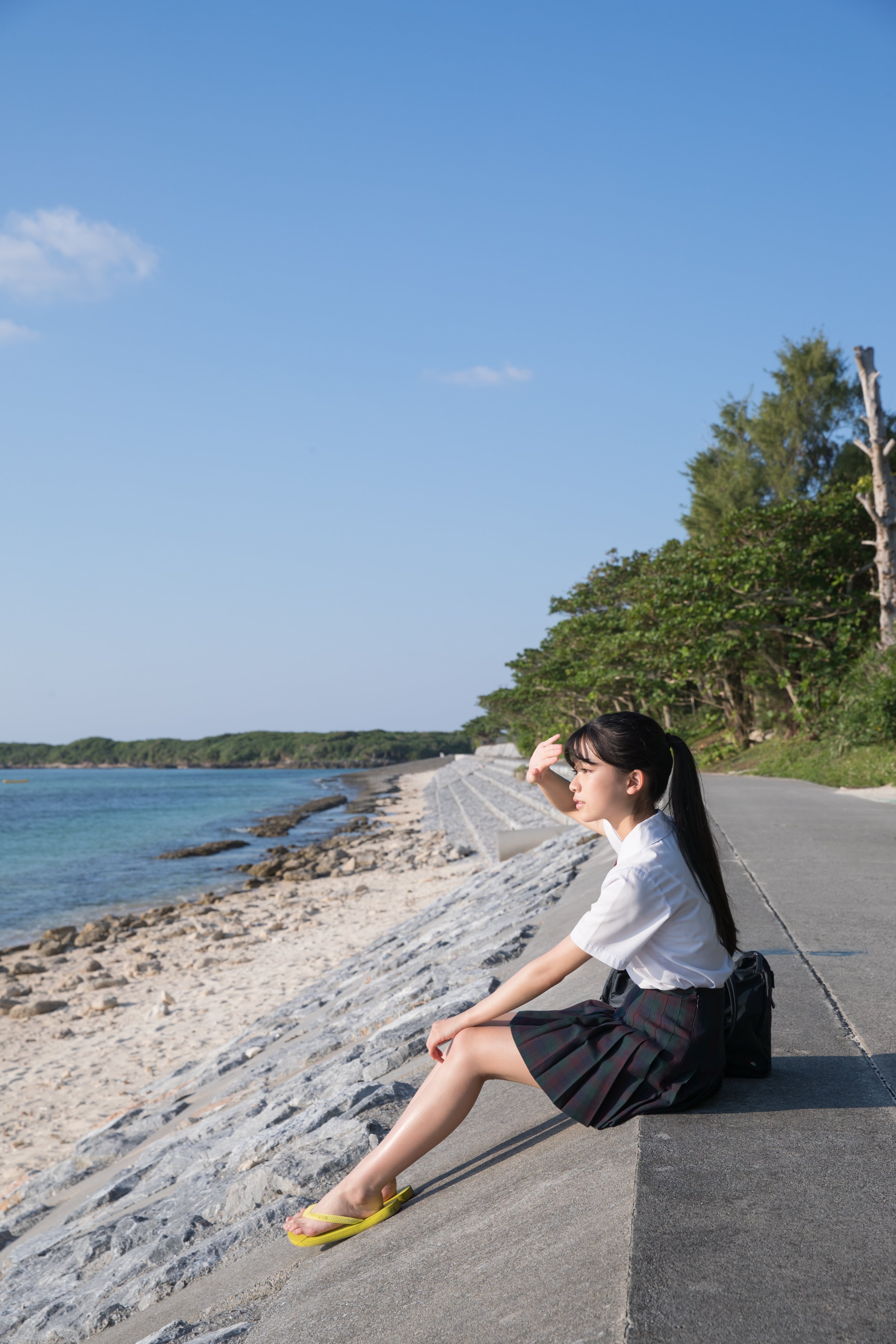 一位穿着一件白色衬衫和一件黑色的裙子的女人坐在俯瞰大海的混凝土墙上。