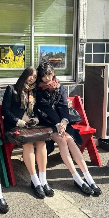 两个女孩坐在一张凳子上,带着一个包围在她的脖子上。