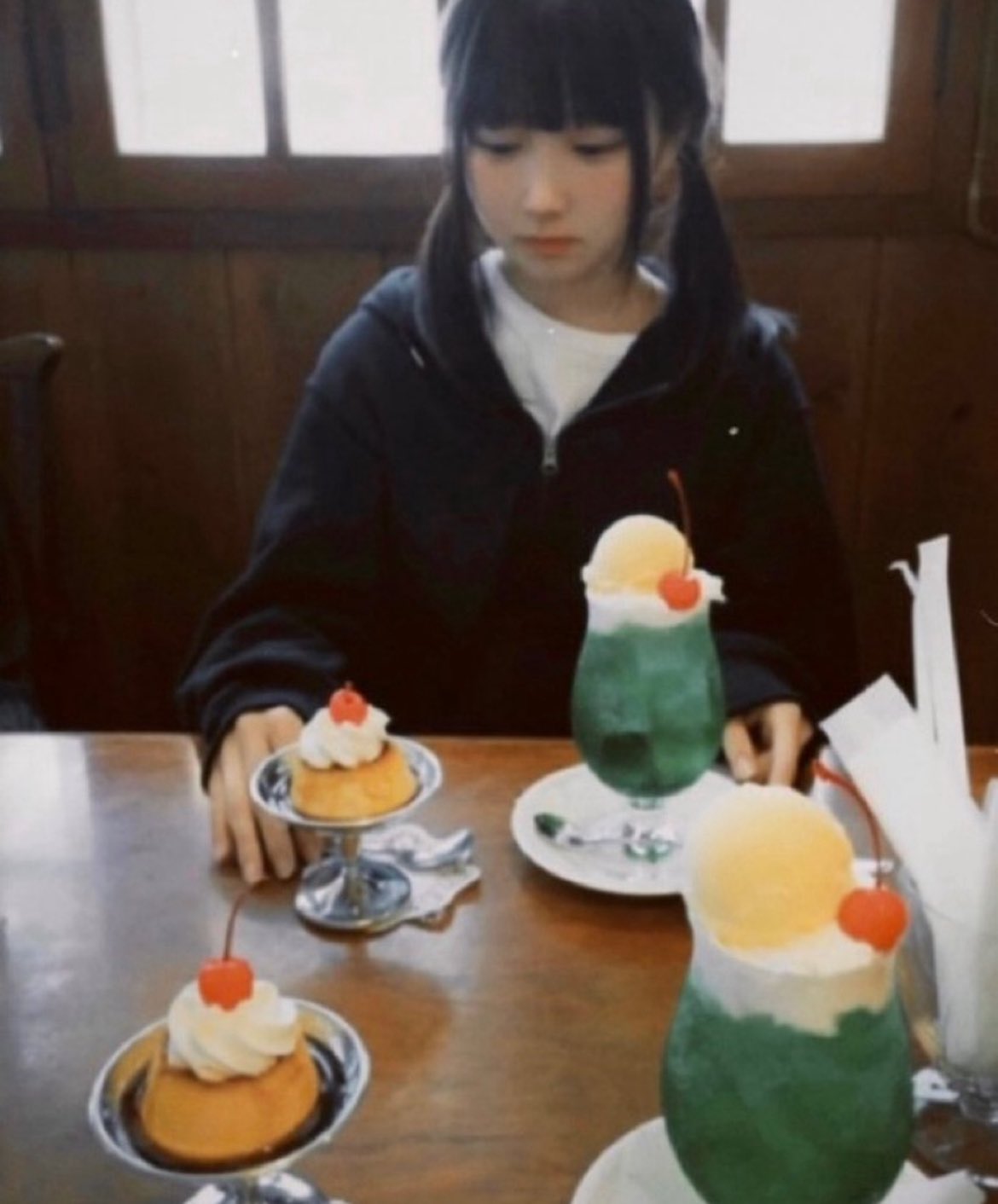 一位穿着黑色夹克和马尾的女孩坐在一张桌子上,在她面前有两个甜点。