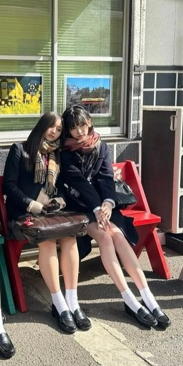 两个女孩坐在一张凳子上,带着一个包围在她的脖子上。