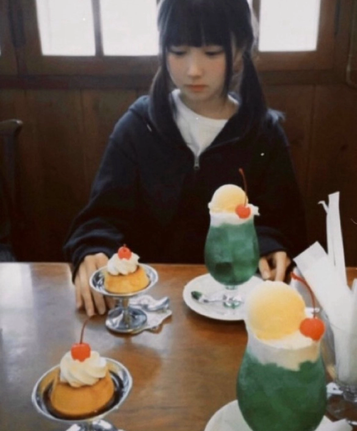 一位穿着黑色夹克和马尾的女孩坐在一张桌子上,在她面前有两个甜点。