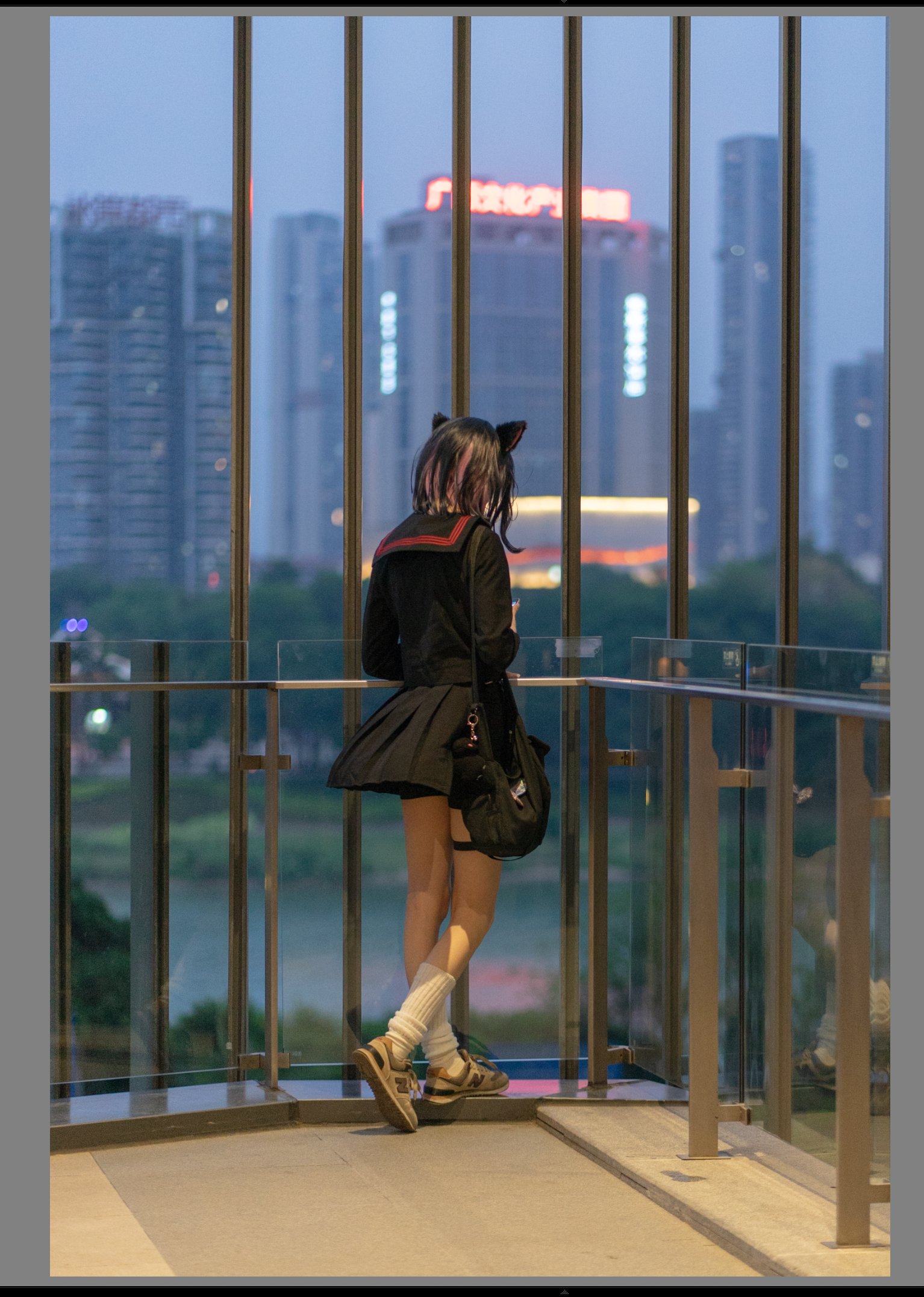 一位戴着猫的耳朵和一件黑色的衣服的女人站在阳台上,俯瞰着一座城市。