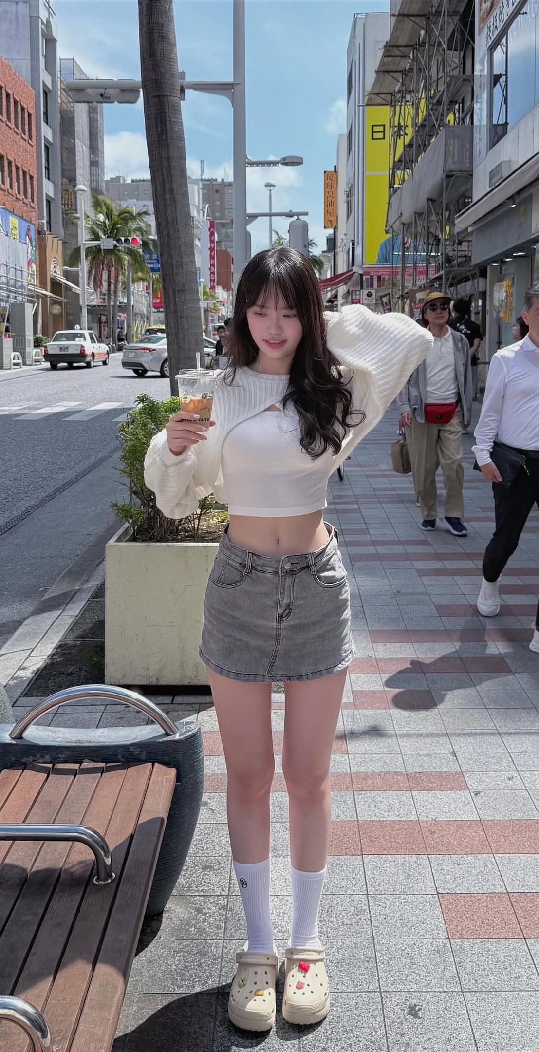 一位穿着白色衬衫和蓝色短裤的女人拿着一杯酒,站在走廊上。