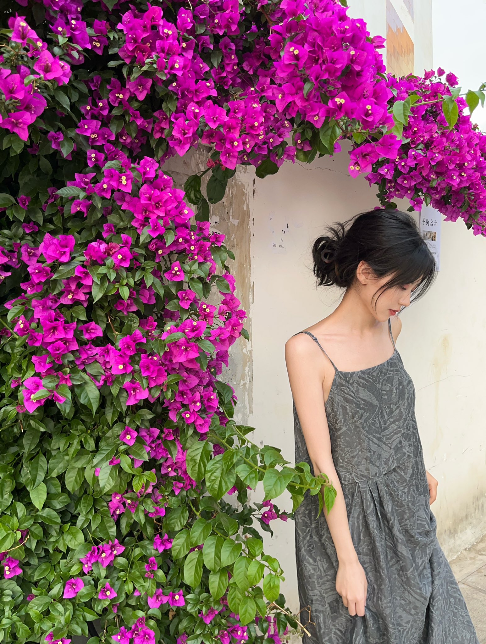 女人站在一堵紫色花的墙前。