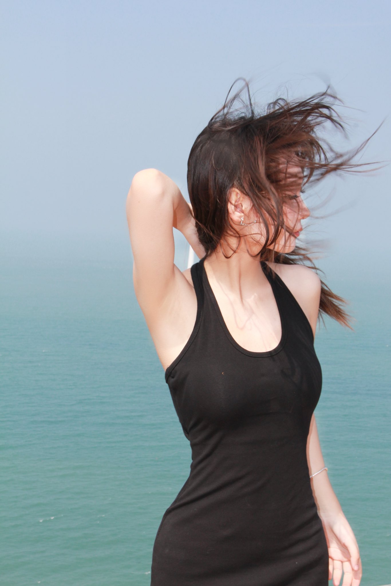 一位黑头发和黑裙子的女人站在一座俯瞰大海的磐石上。