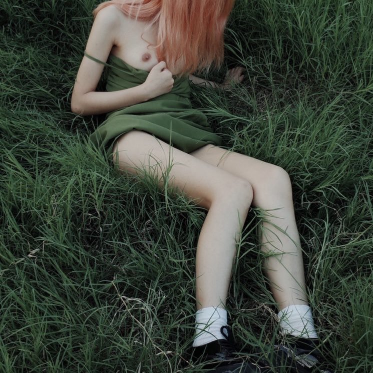 一位穿着粉红色衬衫和绿色裙子的女人坐在草地上。