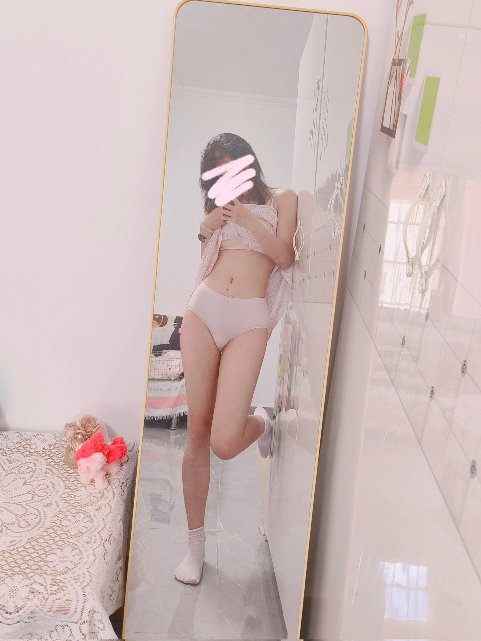 穿着白色胸罩和粉红色的裤子的女人站在镜子前。