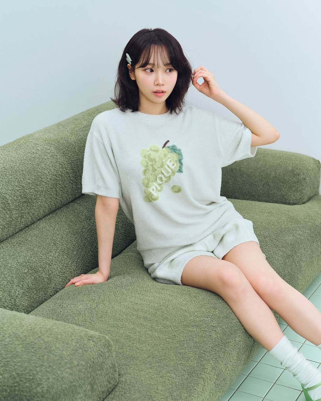 女人穿着一件白色衬衫,上面有绿葡萄,坐在沙发上。