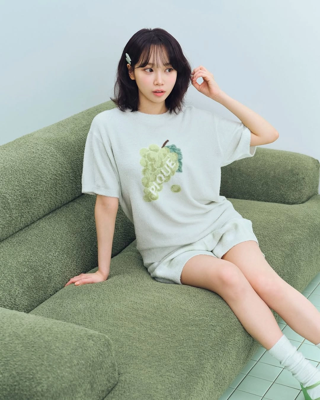 女人穿着一件白色衬衫,上面有绿葡萄,坐在沙发上。