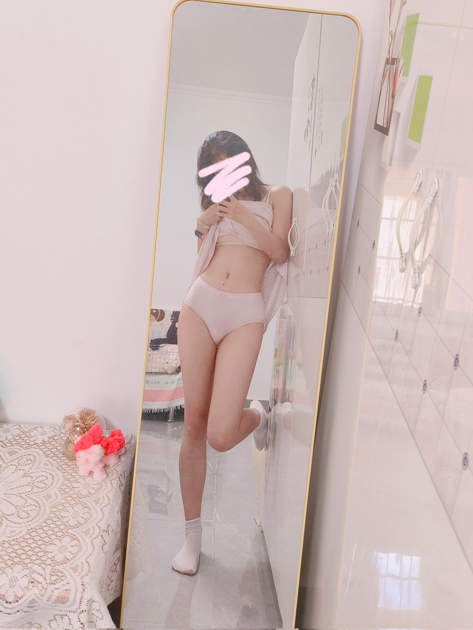 穿着白色胸罩和粉红色的裤子的女人站在镜子前。