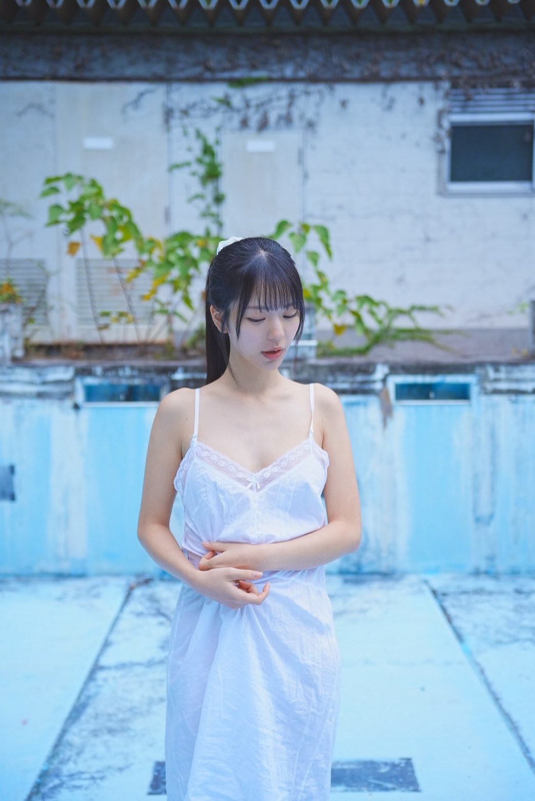 穿着白色裙子的女人站在游泳池前面。