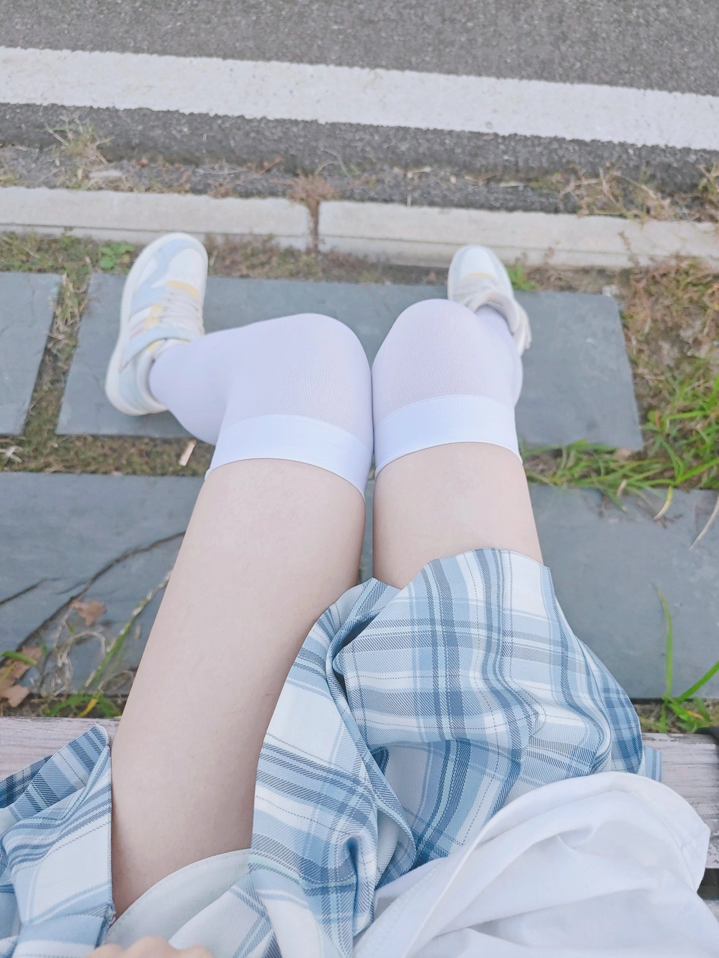 穿着白色裙子和白色袜子的女孩坐在一个凳子上。