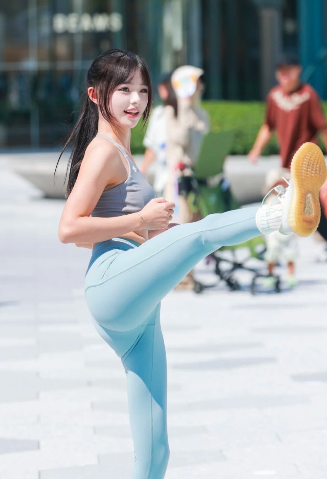 女人穿着灰色坦克顶部和蓝色子踢她的腿。