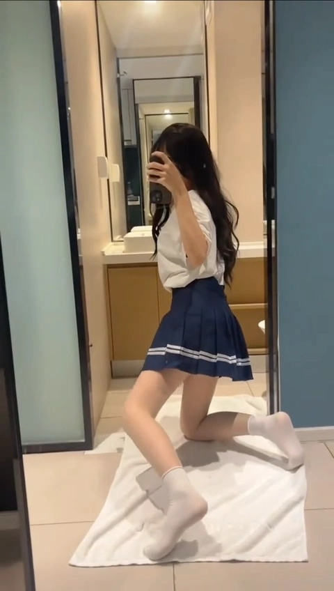 一位穿着蓝色裙子和白色衬衫的女人在浴室镜子里拍了一张自拍。