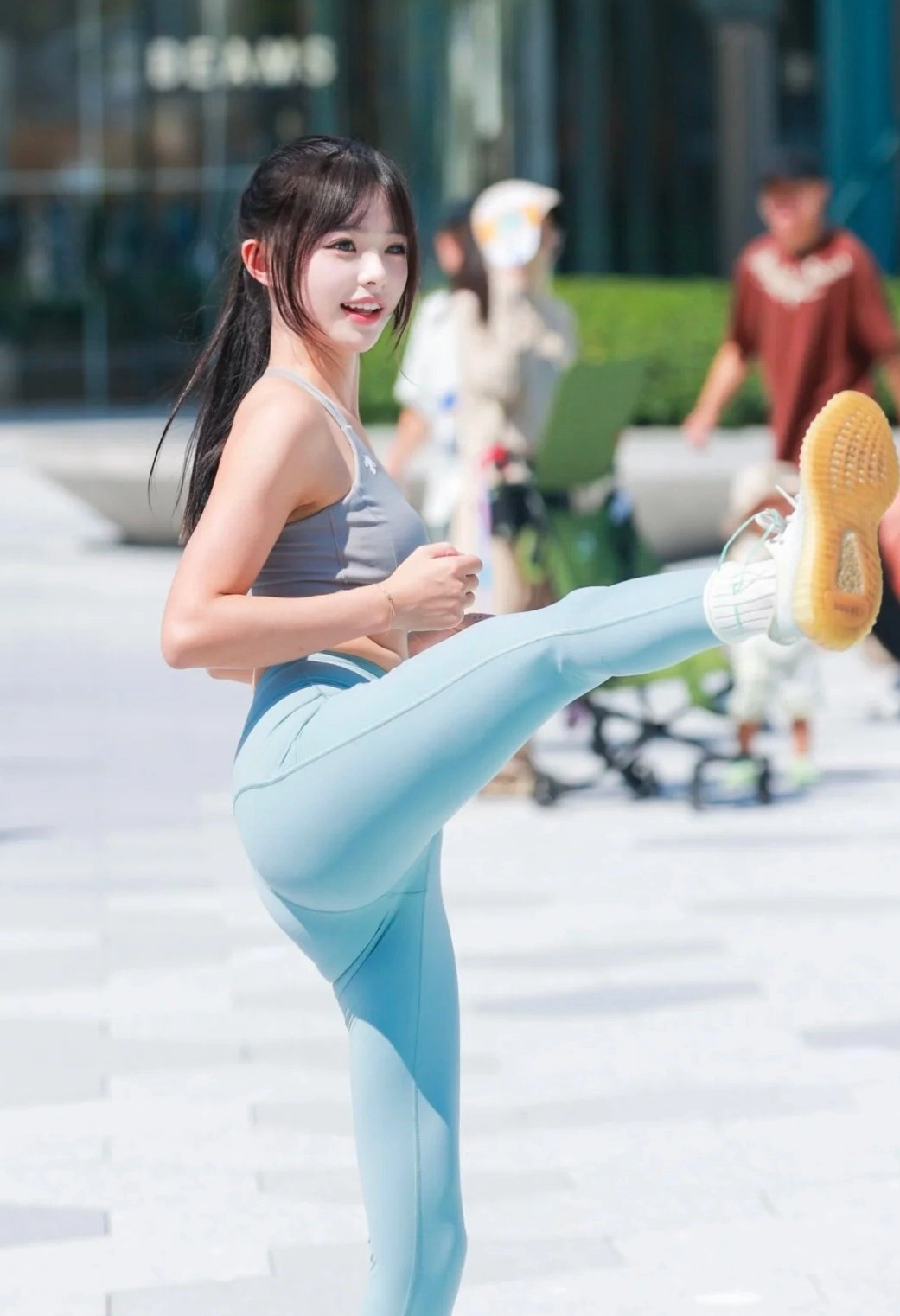 女人穿着灰色坦克顶部和蓝色子踢她的腿。