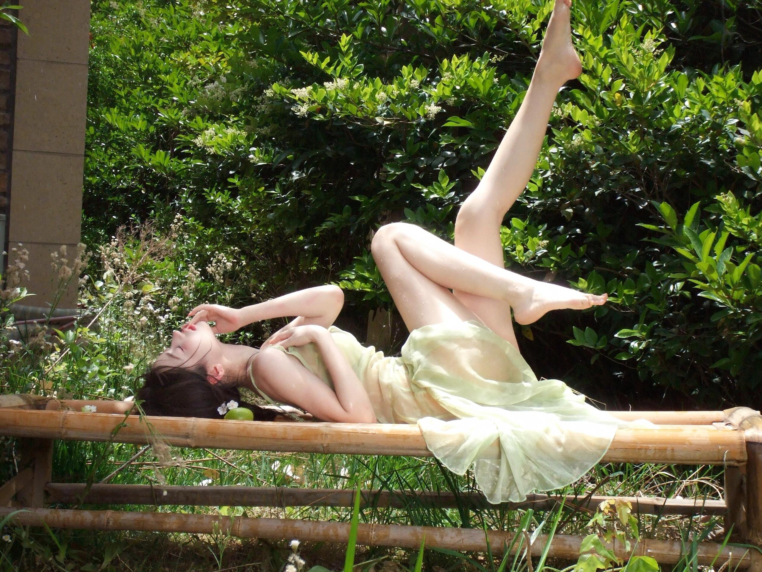 一位穿着绿色衣服的女人坐在一张带一碗水果的凳子上。