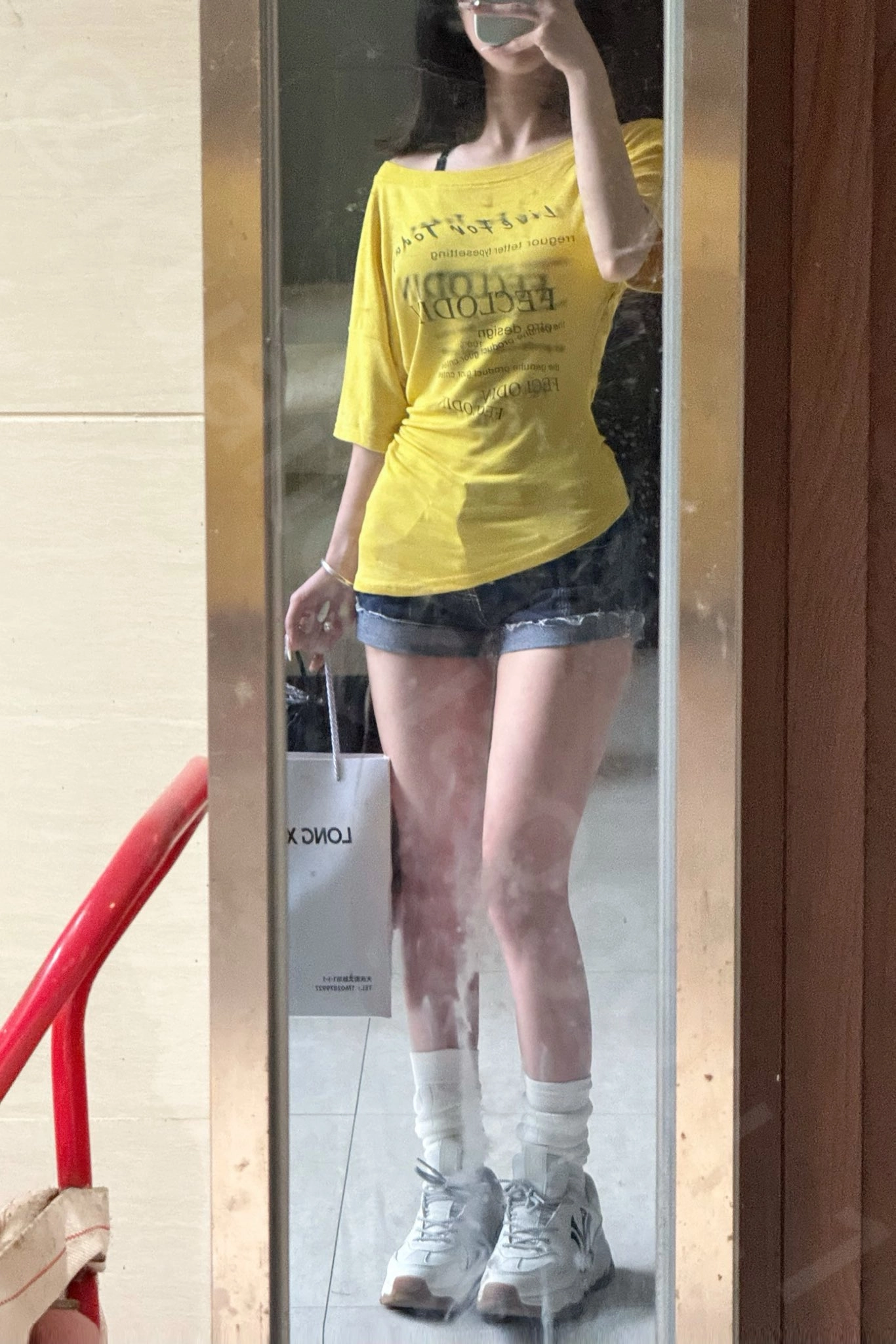 穿着黄色衬衫和短裤的女人在镜子前拍自拍。