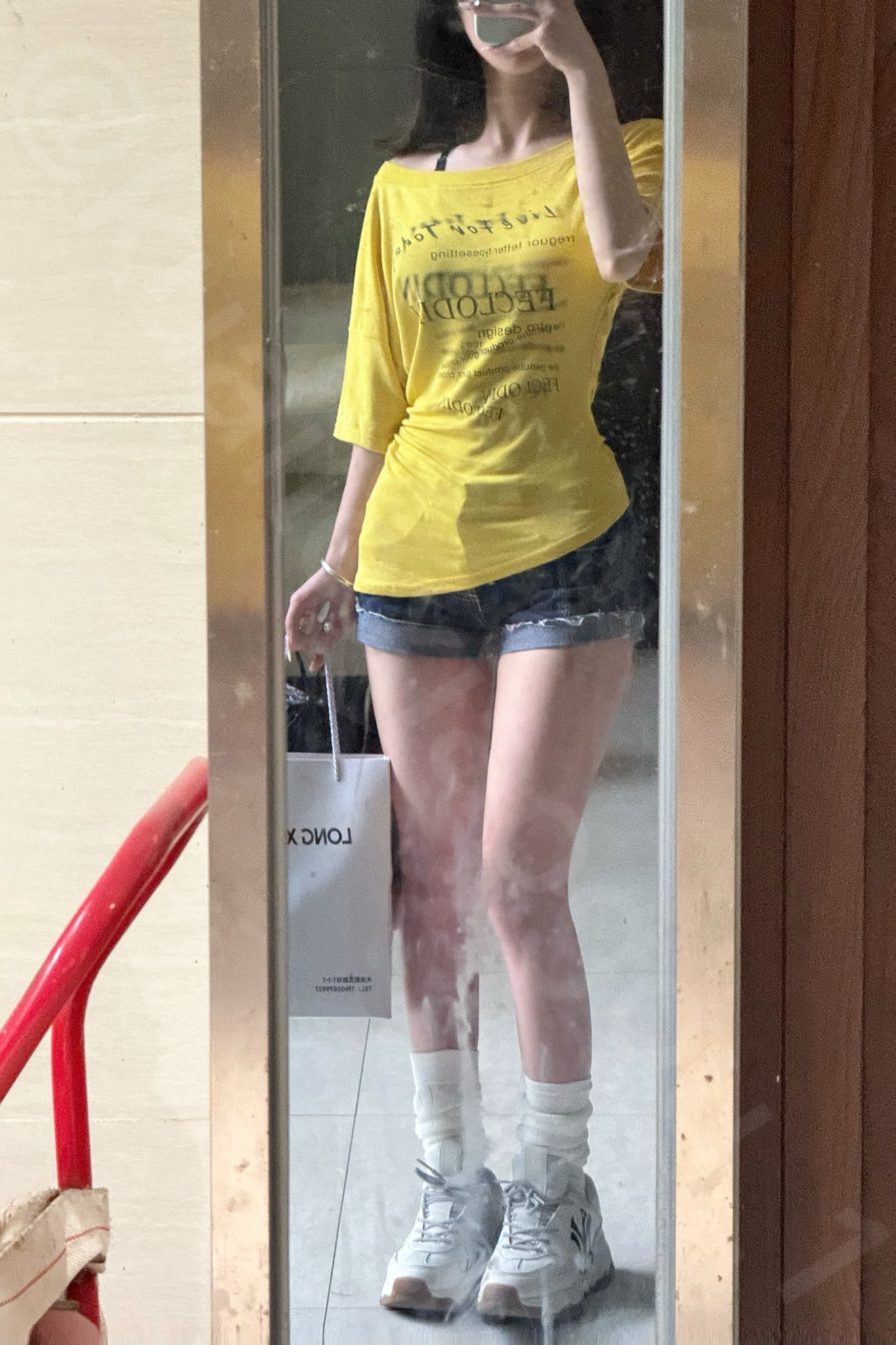 穿着黄色衬衫和短裤的女人在镜子前拍自拍。