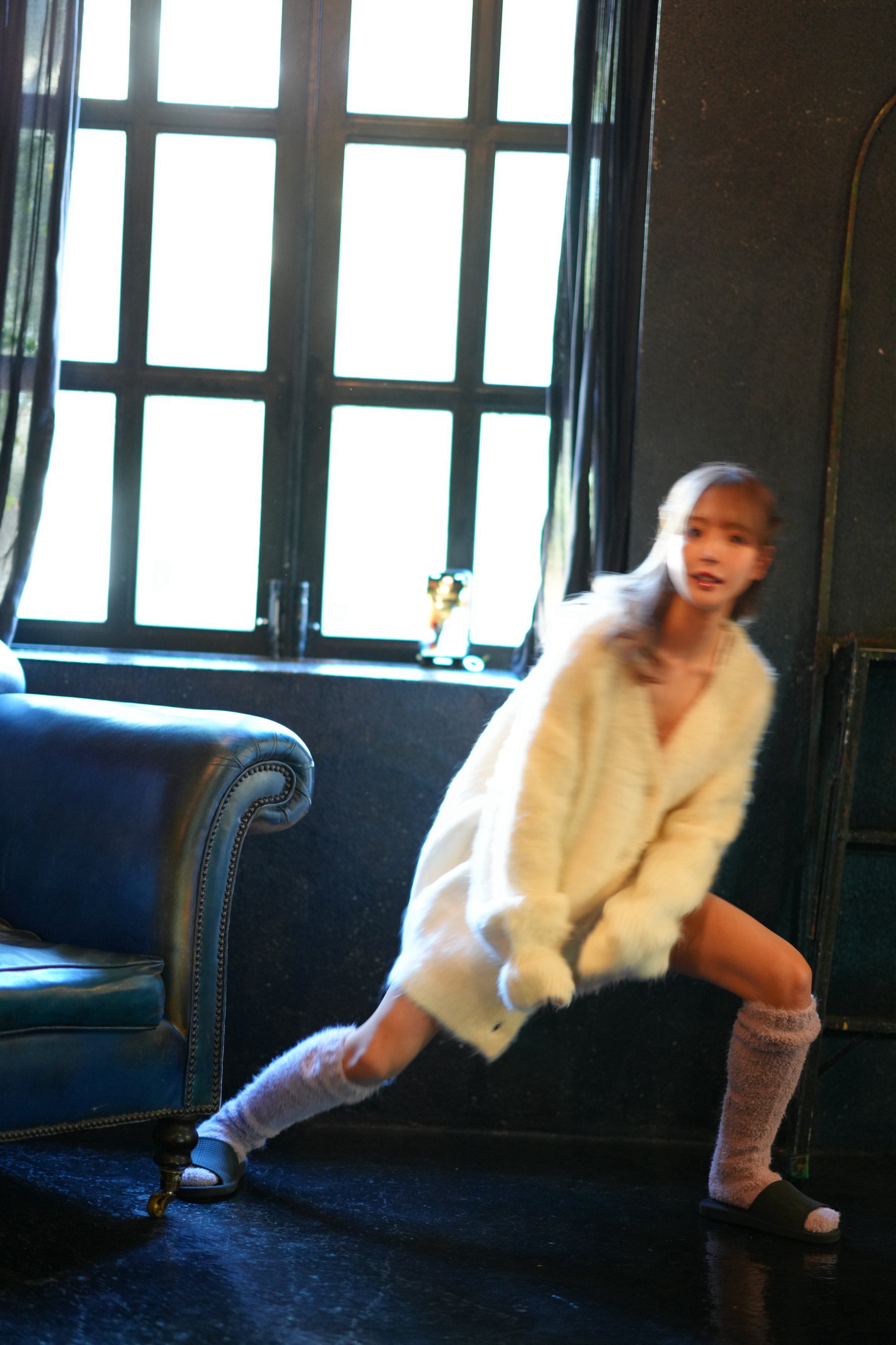 穿着白色外套的女人站在窗前。