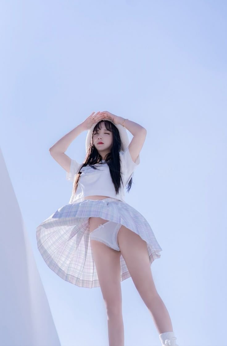 女人穿着白色衬衫和一个的裙子,她的手放在她的头上。